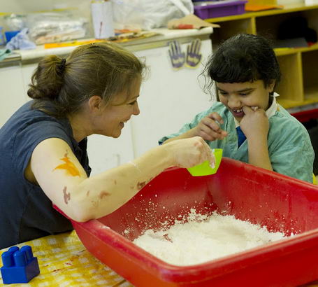 a female teacher and a young autistic
boy play with a red container filled with white flour