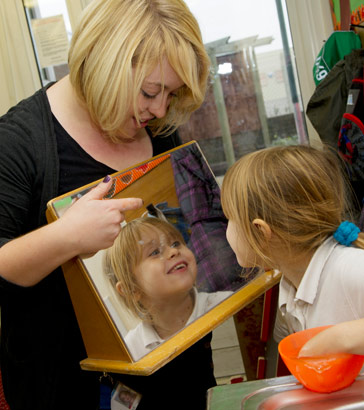 A girl looks at her reflection in
                  a mirror