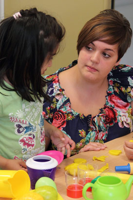 A girl and her teacher at a table with various
                  colourful kitchen-related objects