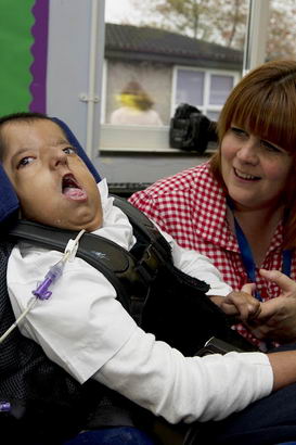 A young boy in a supportive chair
holds one of the finger's of his teacher's hand