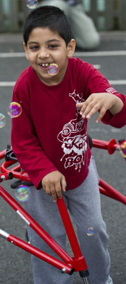 boy reaches for a small green toy held
by a teacher