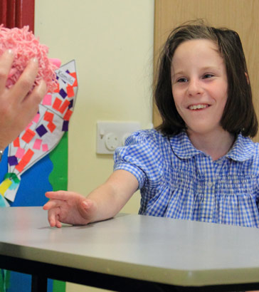 A girl smiles as a teaching sitting opposite
her holds up an object