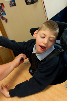 A boy in a specialist chair interacts
with a teacher