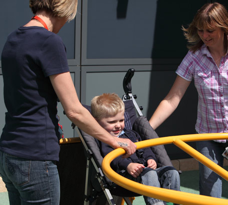 A smiling boy sits in a playground with
                  two women