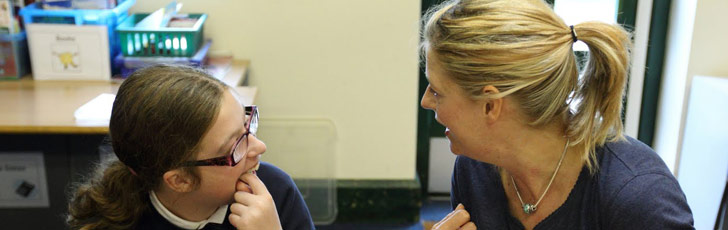 A girl and her teacher sit at a table and
                  communicate