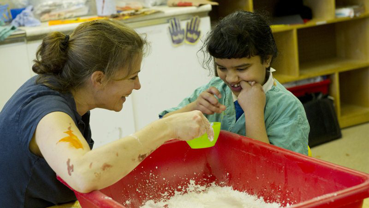 A girl smiles as her teacher
holds a plastic cup over a container of white powder