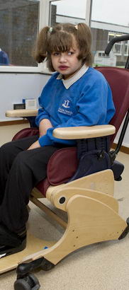 A young girl sits in a supportive
chair whilst her female teacher straps down her feet