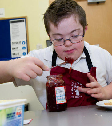 boy in cooking class spooning
                  jam out of a jar