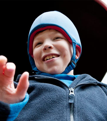 oung boy in protective headgear smiling
                  with teacher/assistant