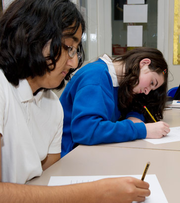 A young girls takes a test alongside
her teacher using a personal computer