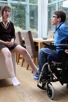 twin brother (in wheelchair) and sister talk
                  to each other in the conservatory of their home