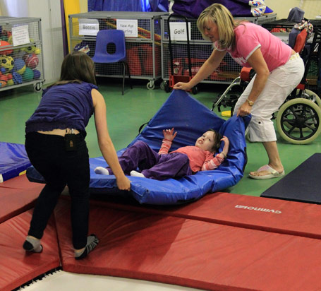 A child being lifted on a mat by two carers