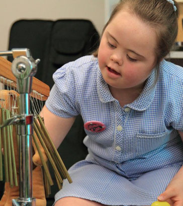 a girl looks at and touches a toy animal
                  held by a teacher