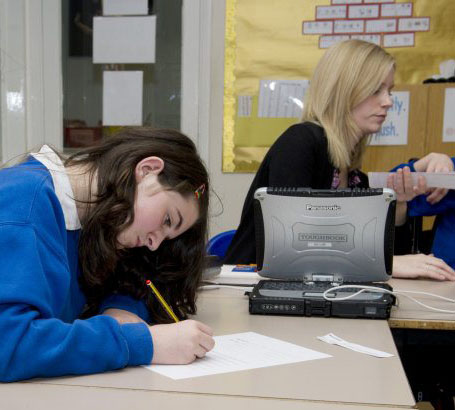 Young boy and teacher sit together whilst
                  pupil writes a plan