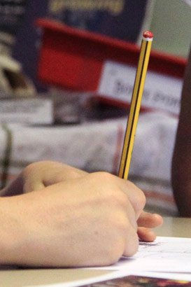 Young boy and teacher sit together whilst
                  pupil writes a plan