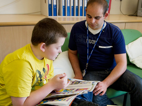 a child sits on a sofa reading
with his caregiver