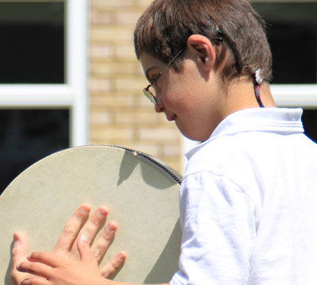 Teacher and boy enjoy playing with a tambourine
on a school's lawn