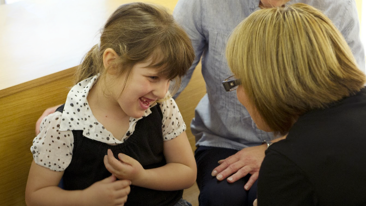 A seated girl smiles as a teacher
talks to her