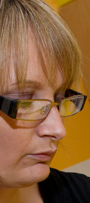 a teacher wearing glasses sits
at a table taking notes on one of her pupils