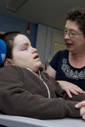 A carer holds the hand and arm
of a boy in a specialist chair