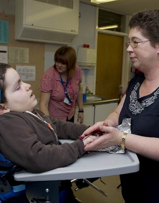 A carer holds some foil in the
hand of a boy in a specialist chair