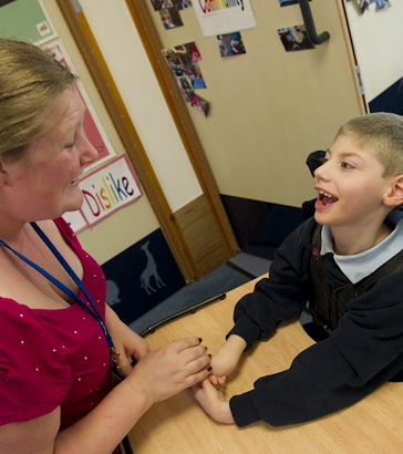 A boy in a specialist chair smiling
with his teacher
