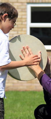 A male teacher and a young boy use a drum
to interact in a school field