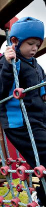 Young boy with protective headgear
                  traverses adventure playground