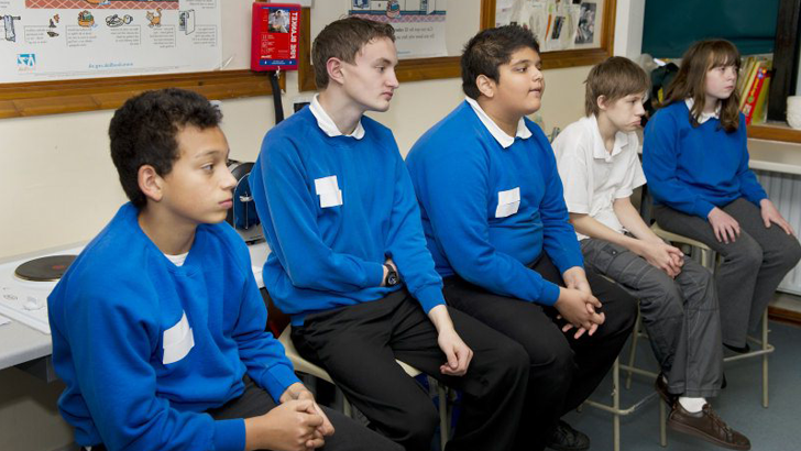 A girl and four boys seated
looking at their teacher