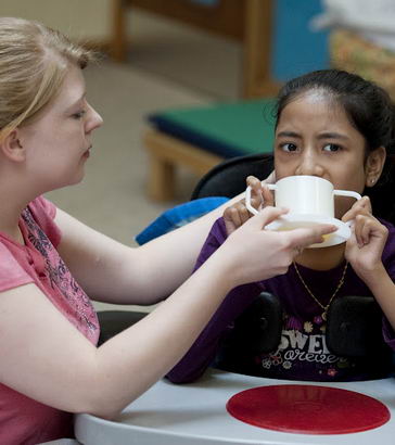 A carer helps a girl drink from
                  a cup