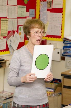 A teacher holds up a self-assessment
                  card depicting a green disc