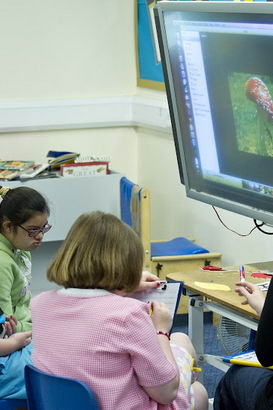 Three pupils and a teacher use
a large touch-screen