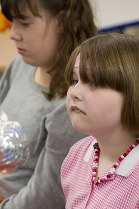 A girl with a keyboard on her
                  lap listens to a teacher