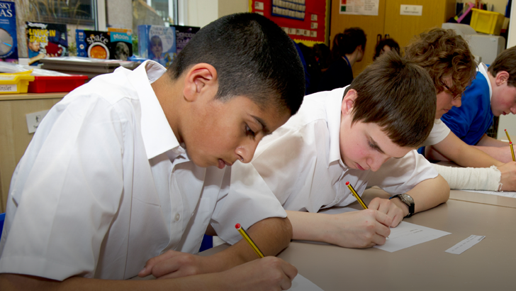 A row of boys writing at a
                  classroom table