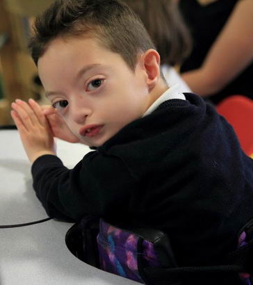 A boy in a standing aid looks at the camera