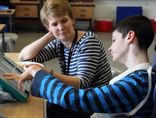 Boy in blue top with glasses relaxed and
                  happy seated opposite his teacher