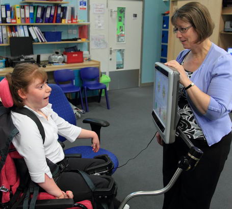 A teacher helps a young girl to communicate
                  using a screen at eye level