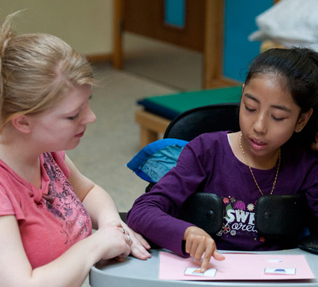 A young girl communicates with
                  her teacher by pointing at symbols