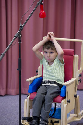 young boy in stripey top and supportive
chair uses aural equipment to communicate