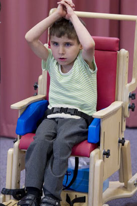 young boy in stripey top and
supportive chair uses aural equipment to communicate