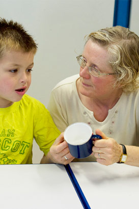 A teacher and a young boy use
a blue mug as an object of reference