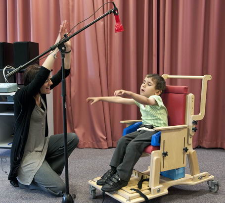 A teacher uses an assistive
device on a microphone stand to communicate with a young boy in a supportive chair