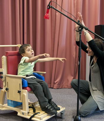 A teacher uses an assistive
                  device on a microphone stand to communicate with a young boy in a supportive chair