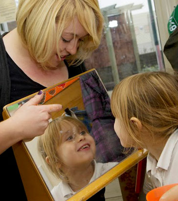 A female teacher holds a mirror
                  in front of a young female student