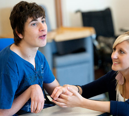 A young female teacher coaxes
a teenage boy to communicate