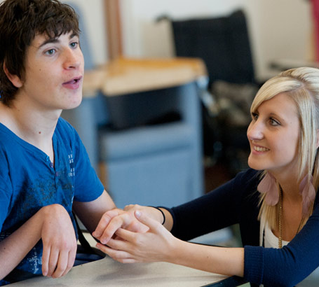 A young female teacher coaxes
a teenage boy to communicate