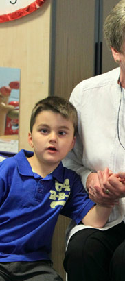 An older female teacher comforts, supports
and holds the hand of a young boy