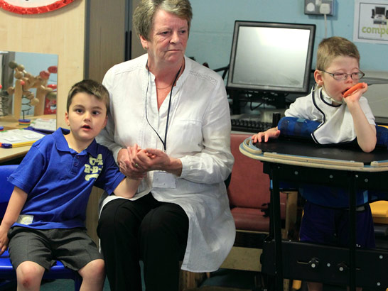 An older female teacher comforts, supports
and holds the hand of a young boy width=