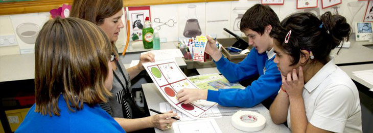 Two lead professionals sat at a classroom
                  desk with five children