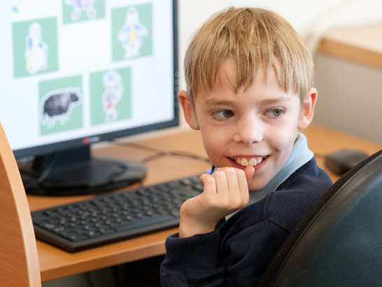 a young boy smiles at the camera
                  as he works on a computer